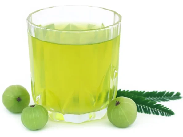 Glass of fresh amla juice with whole Indian gooseberries and green leaf on white background.