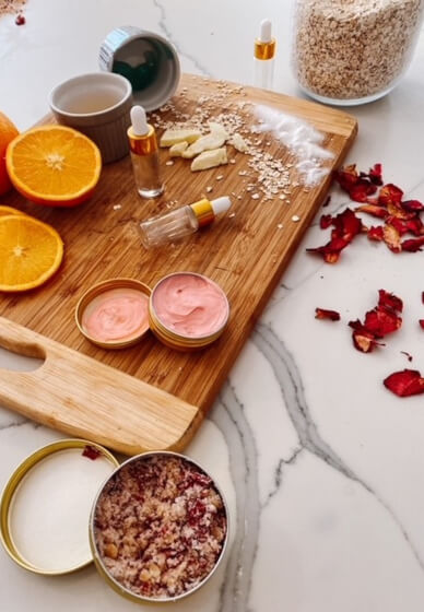 Natural skincare ingredients like oranges, oats, rose petals, and essential oils arranged on a wooden board for a DIY beauty and wellness routine.
