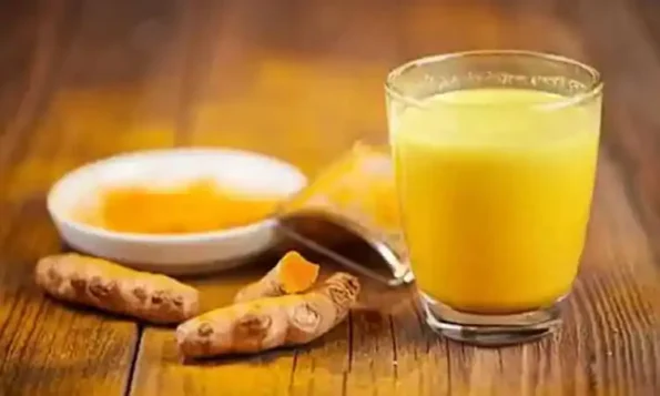 A glass of turmeric milk (golden milk) with raw turmeric roots and turmeric powder on a wooden table.