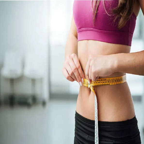 Woman in fitness wear measuring her waist with a measuring tape, symbolizing weight and health tracking.
